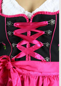 Women's black Dirndl dress with a vibrant pink satin apron, lace-up bodice, white blouse, and traditional Bavarian Oktoberfest styling.