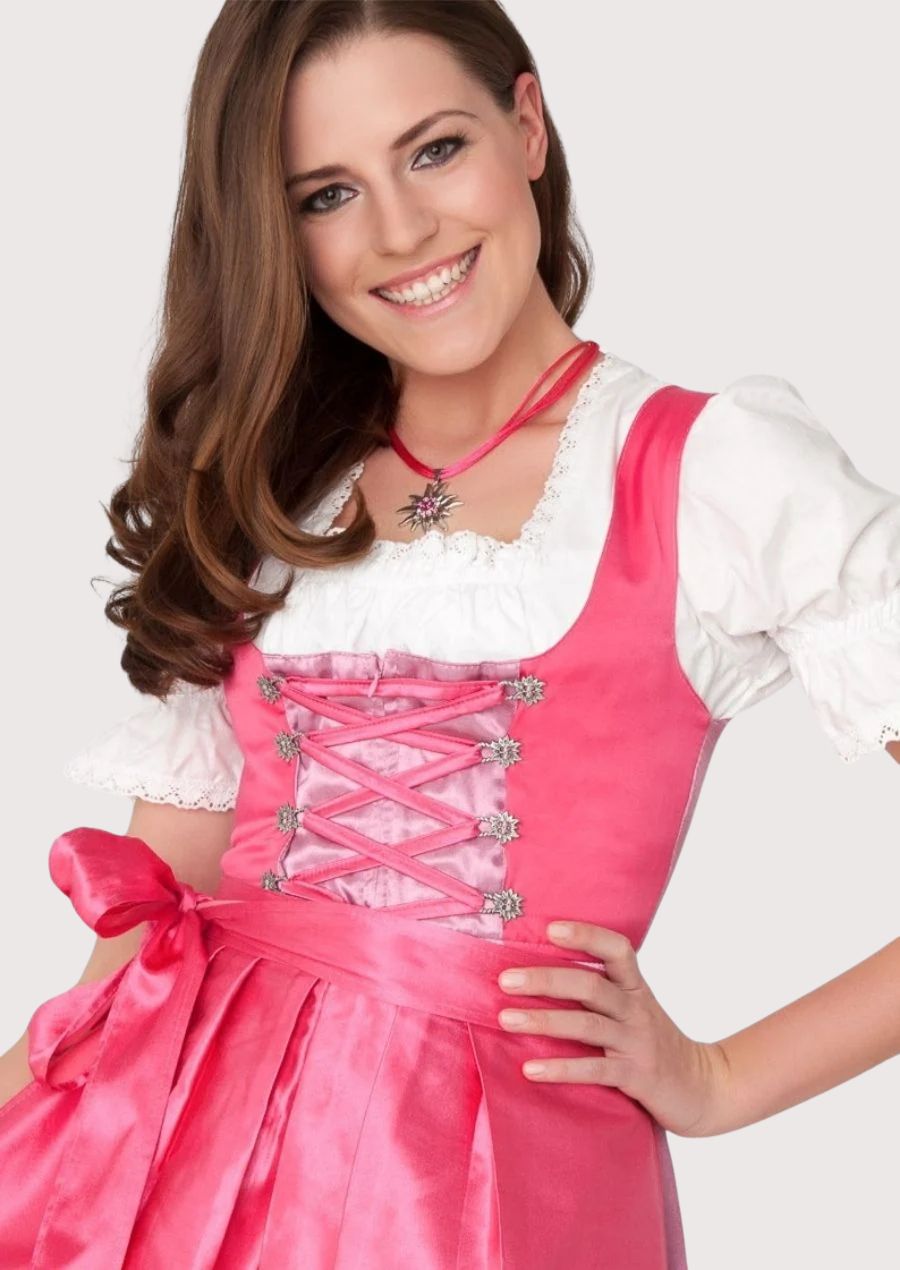 Elegant Bavarian Dirndl featuring a vibrant pink bodice, glossy satin apron, decorative corset lacing, and feminine Alpine craftsmanship.