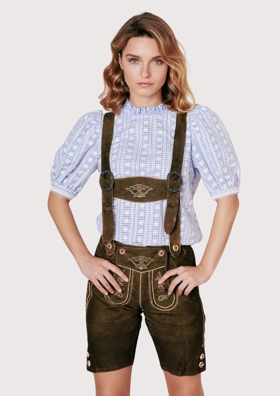 Woman wearing traditional Bavarian lederhosen with blue alpine blouse and embroidered suspenders