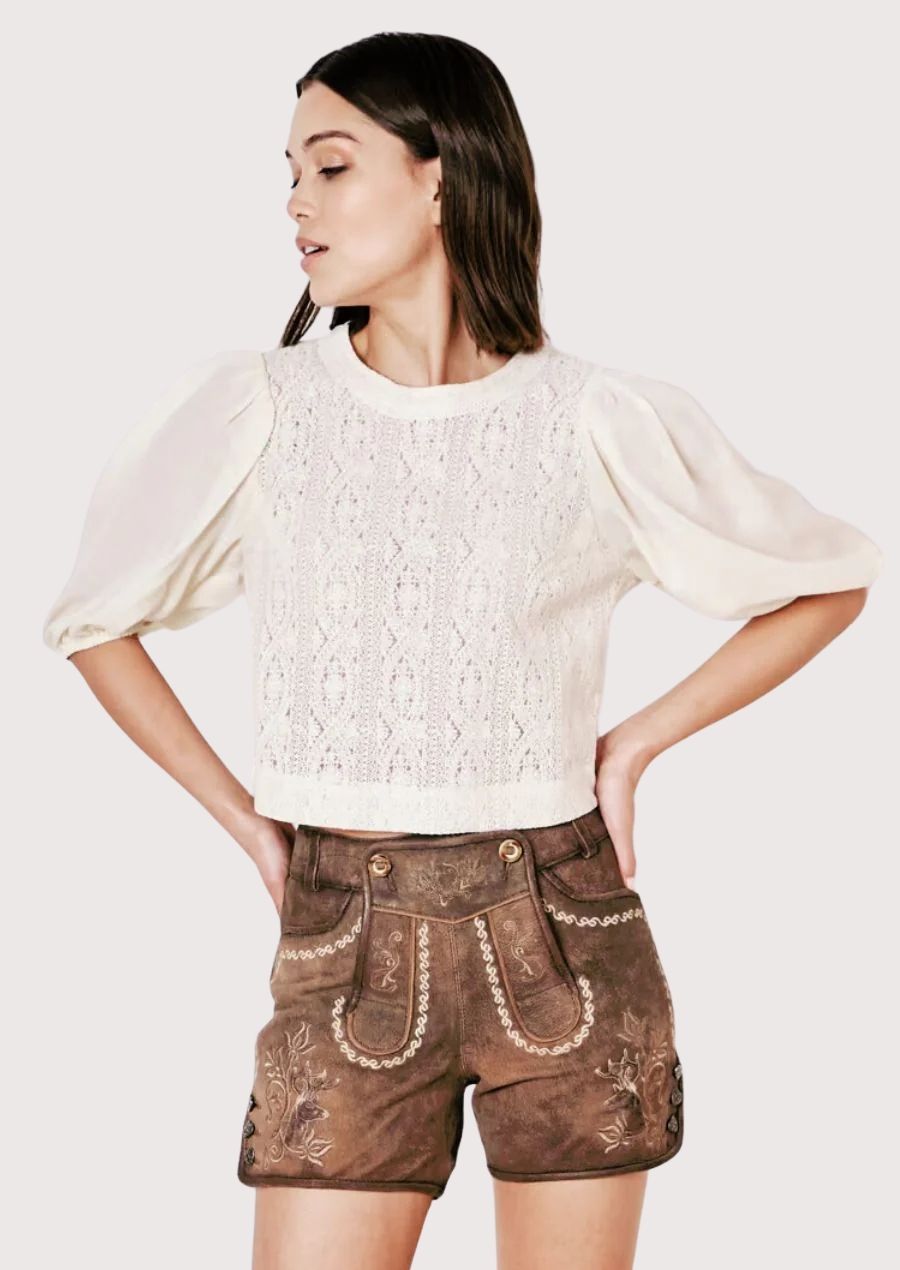 Woman wearing brown embroidered lederhosen paired with cream lace cropped blouse
